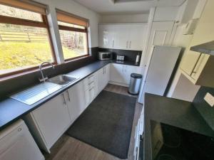 a kitchen with white cabinets and a sink and a window at Altdarroch Farm House in Kinlocheil