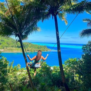 a woman swinging on a rope swing between two palm trees at ALAROOTS HUAHINE in Haapu