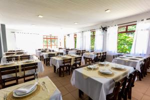 アグアス・デ・リンドイアにあるHotel Fazenda Aguas de Lindoiaの白いテーブルと椅子、窓のあるレストラン