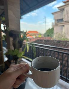 une personne tenant une tasse de café sur un balcon dans l'établissement Yudis Guest House, à Ubud