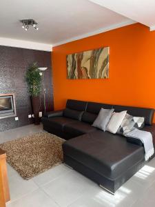 een woonkamer met een zwarte bank en een oranje muur bij Passagem Pro Mar in Valado dos Frades
