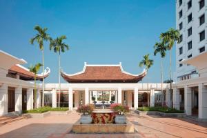 a building with a fountain in a courtyard with palm trees at Sheraton Hanoi Hotel in Hanoi