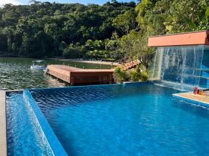 a swimming pool with a waterfall next to a body of water at Pousada e Restaurante Mangue Seco Angra in Angra dos Reis