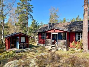 a red cabin with a porch in the woods at Holiday home ORNÖ II in Dalarö