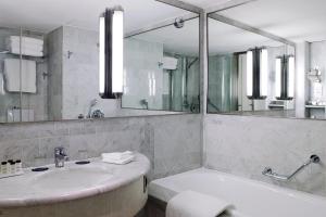 een badkamer met een wastafel, een bad en een spiegel bij Sheraton Paris Charles de Gaulle Airport Hotel in Roissy-en-France