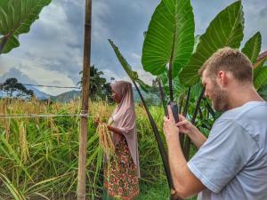 een man die een foto neemt van een vrouw in een veld bij Farmstay Manangel in Sindanglaka