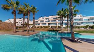 - une piscine bordée de palmiers en face d'un bâtiment dans l'établissement Las Colinas Golf, luxury penthouse, à Orihuela