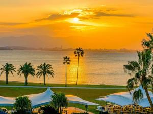una puesta de sol sobre el agua con palmeras y sombrillas en The Luigans Spa and Resort, en Fukuoka