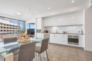 een keuken met witte kasten en een glazen tafel bij Luxury 1BR Apartment @ Harbour Lights Cairns in Cairns