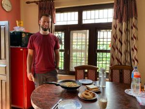 a man standing in a kitchen with a pan on a table at Panauti Homestay in Panauti