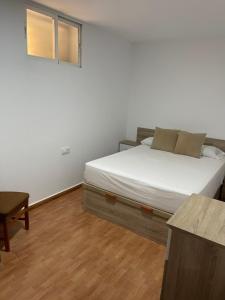 a bedroom with a bed with white sheets and a table at Vivienda Fines Turísticos La Victoria in Jaén