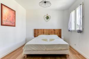 a white bedroom with a bed with a wooden headboard at La Villa d'Isa et Seb in Narbonne