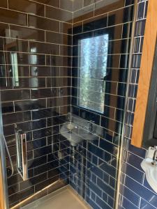 y baño con ducha de azulejos negros y lavamanos. en Cosy Shepherd's Hut near Shrewsbury, 