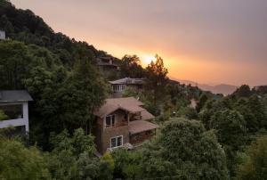 a house in the trees with the sunset in the background at SaffronStays Plaksha - 2BR pet-friendly homestay with Himalayan views, verandah dining & bonfire near Chauli ki Jali in Mukteshwar +30 photos