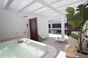baño blanco con bañera y planta en Sa Pedrera Suites & Spa, en Es Pujols