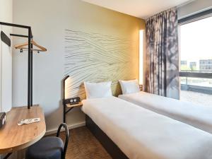 a room with two beds and a desk and a window at B&B HOTEL Argenteuil in Argenteuil