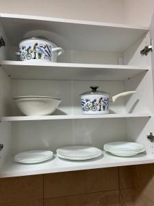 a white kitchen with plates and bowls on shelves at Tik-tak apartment in Petrovaradin