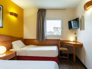 a hotel room with two beds and a desk and a window at B&B HOTEL Strasbourg Nord Mundolsheim in Mundolsheim