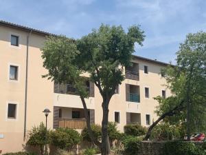 um prédio de apartamentos com uma árvore em frente em Appartement dans résidence avec piscine et parking em Uzès