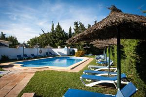 a pool with chairs and a straw umbrella at Hostal Cabo Roche in Conil de la Frontera