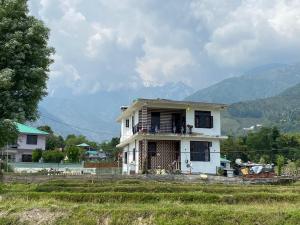 a white house in a field with mountains in the background at DHAULADHAR HOMESTAY PALAMPUR in Pālampur