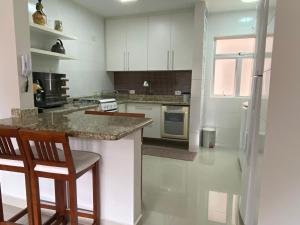 a kitchen with white cabinets and a counter with chairs at Apto todo equipado em Caiobá há 50m do mar in Matinhos