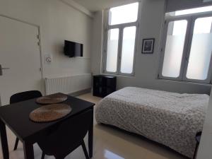 a bedroom with a bed and a table and windows at Résidence Jehan Froissart in Valenciennes