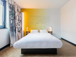 Cette chambre dispose d'un grand lit blanc et d'un mur jaune. dans l'établissement B&B HOTEL Sélestat Centre-Alsace, à Sélestat