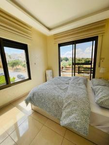 a bedroom with a large bed and two windows at Amman Sun Apartments in Ţāb Kirā‘