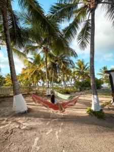 a person laying in a hammock on a beach with palm trees at Pousada o Forte in Mangue Sêco