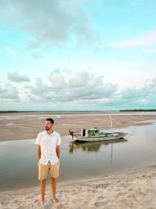 um homem parado na praia ao lado de um barco em Pousada o Forte em Mangue Seco