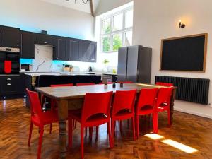 a kitchen with a wooden table and red chairs at Bodham School Halls - 5 Bedrooms in Bodham