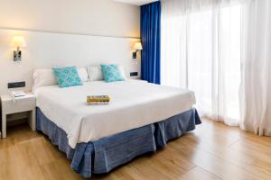 a bedroom with a large white bed with blue pillows at Mar Hotels Alcanada in Port d'Alcudia