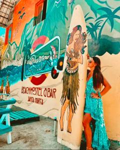 two girls standing next to a surfboard in front of a mural at Playa del Ritmo Beach Hostel & Bar - Adults Only in Santa Marta