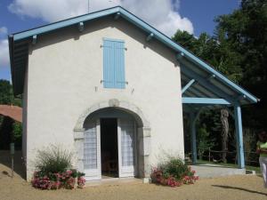uma pequena capela branca com uma janela azul e flores em Gite arriou du bruca em Sort-en-Chalosse