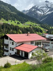 un edificio con techo rojo con montañas al fondo en alpenHIRSCH - Ferienwohnungen, en Hirschegg