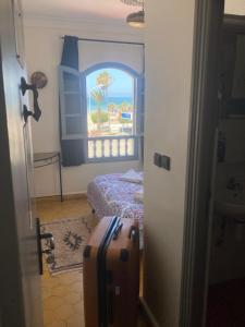 um quarto com uma cama, uma janela e uma mala em Essaouira Beach Hostel em Essaouira