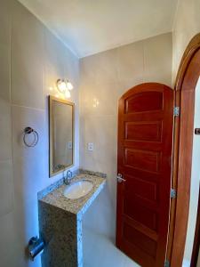 baño con lavabo, espejo y puerta en Pousada Paraíso dos Corais, en Arraial do Cabo