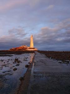 a lighthouse on a beach with a pathway leading to it at AzZule - Tynemouth in Tynemouth
