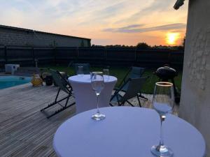 two tables with wine glasses on a deck with the sunset at Maison de ville atypique in Le Molay-Littry