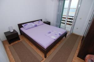 a bedroom with a bed with purple pillows and a balcony at Apartments Kraj, Tratica Beach in Kraj