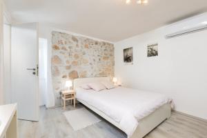 a bedroom with a white bed and a stone wall at Guest house Otto in Punat