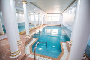 a large indoor pool with blue water and columns at The Amsterdam Boutique Hotel in Aktobe
