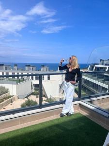 una mujer de pie en un balcón bebiendo de una botella en Gran Apartment-Iconic Sea View, en Gran Alacant
