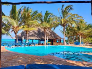 a resort swimming pool with palm trees and the ocean at Queen of Sheba Beach Lodge in Pongwe