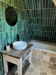 een groene betegelde badkamer met een wastafel en een bad bij Gîte le Terrier in Hotot-en-Auge