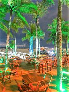 a group of tables and chairs on a beach with palm trees at Pousada Primeira Quadra Da Praia in Praia Grande