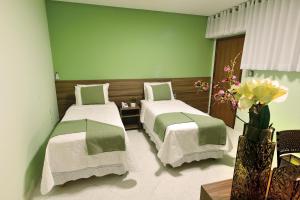 two beds in a room with green walls and flowers at Domus Hotel Cidade Nobre Ipatinga in Ipatinga