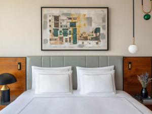 Una cama con almohadas blancas y una pintura encima. en Swissotel Living Jeddah en Yeda