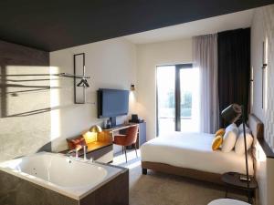 a bedroom with a tub and a bed and a television at Mercure Namur Hotel in Namur